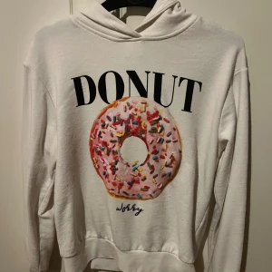 Vit hoodie med donut-tryck från ONLY - Vit hoodie från ONLY i storlek S med stort färgglatt donut-tryck och texten 'DONUT WORRY' på framsidan. Tröjan har huva, långa ärmar och är gjord i mjuk bomull. Perfekt för dig som gillar roliga prints och chill stil.
