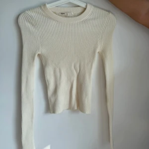 Ribbad vit långärmad tröja Pull&Bear - Säljer en ribbad vit långärmad tröja från Pull&Bear i storlek S. Tröjan har en rund halsringning och är figurnära med stretchigt material. Perfekt för lager-på-lager och passar till jeans eller kjol. Enkel och stilren design som är lätt att matcha.