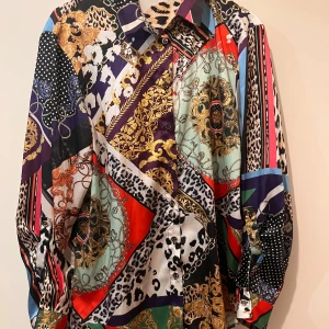 Skjorta strl 38 - Skjorta strl 38 från River Island.  Mycket fint skick. Det enda är att trådar gått upp på två ställen, se alla bilder. Syns knappt eftersom tyget har så många färger och mycket mönster. Guldfärgade knappar och möjlighet till att ha trekvart ärm. Material: polyester 