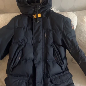 Mörkblå dunjacka Parajumpers S - Säljer en svart dunjacka från Parajumpers i storlek S. Jackan har huva, flera fickor med dragkedja och tryckknappar samt den klassiska gula detaljen vid halsen. Perfekt för kalla dagar och riktigt snygg streetstil. Kan dusketera om priset vid snabbaffär 