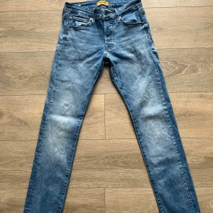 Blå slim fit jeans från Jack & Jones - Säljer ett par blå slim fit jeans från Jack & Jones i modellen JIGLENN. Jeansen har klassisk femficksdesign, snygga slitningar och normalhög midja. Tillverkade i mjukt denimtyg med dragkedjegylf och snygga kontrastsömmar.