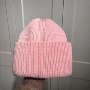 Ljusrosa ribbad mössa med satin - Säljer en ljusrosa ribbstickad mössa med bred uppvikt kant. Insidan är fodrad med glansigt rosa satin, vilket gör den extra skön och skonsam mot håret. Perfekt för kalla dagar och en snygg detalj till din vinterstil. Lite smink på satinen!🩷
