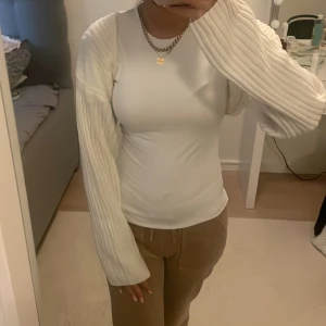 Vit ribbad långärmad tröja - Säljer en vit långärmad tröja med ribbade ärmar och kropp. Tröjan har en slim passform och är tillverkad i ett mjukt stickat material som sitter snyggt på kroppen. Perfekt för dig som gillar stilrena och enkla plagg med lite extra struktur på ärmarna.