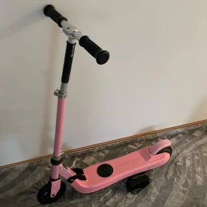 Booster Scooter Pink - Elektrisk kickbike i rosa färg, modell Booster Scooter. Justerbar styre, laddare medföljer. Skicket ser bra ut med minimalt slitage, inga synliga defekter. Perfekt för barn eller ungdomar som vill ha en smidig och rolig transport. Information Motoreffekt: 100 W Maxhastighet: 4–6 km/h Maxvikt: 50 kg Räckvidd: Upp till 6 km Laddningstid: 2–2,5 timmar. Pris: Buda gärna