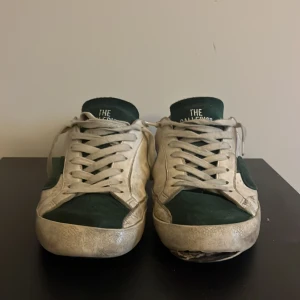 Vita och gröna sneakers The Galleryist - Ett par vit gröna skor från the galleryst! Storlek 42. Ganska sliten på baksida sulan och på framsidan. Box följer med på köp! Perkeft för dig som vill lägga en liten touch på sin outfit. Kontakta om frågor och pris kan diskuteras🤝