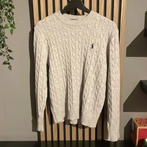 Polo ralph Lauren kabelstickad - Säljer en klassisk ljusgrå stickad tröja från Ralph Lauren med kabelstickat mönster och broderad logga på bröstet. Passar dig som är runt 160-170!   Kan självklart gå ner i pris vid snabb och smidig affär! 😁