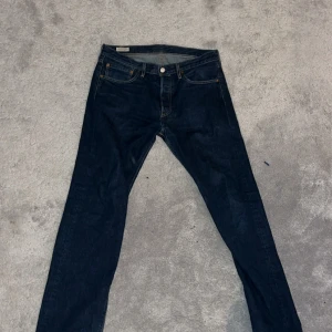 Levi's 501 mörkblå jeans W31 L32 - Klassiska Levi's 501 jeans i mörkblå tvätt med raka ben och fem fickor. Snygga kontrastsömmar och ikonisk läderpatch bak i midjan. Jeansen har normal passform och är tillverkade i slitstarkt bomullsjeansmaterial. Perfekta för dig som gillar tidlös stil.