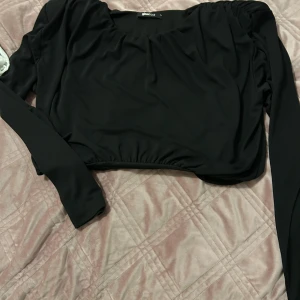 Svart långärmad topp Gina Tricot - Säljer en svart långärmad topp från Gina Tricot med croppad passform och lätt rynkade detaljer vid axlar och midja. Toppen har en rundad halsringning och är tillverkad i ett mjukt, stretchigt material som sitter snyggt på kroppen.