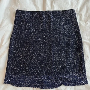 Mörkblå glittrig kjol - Supersnygg mörkblå kortkjol täckt med glittrande paljetter. Kjolen har en rak passform och är perfekt för dig som vill sticka ut med en festlig look. Materialet är mjukt och följsamt, vilket gör den bekväm att bära hela kvällen. Perfekt inför nyår! Använd endast 1 gång 💙