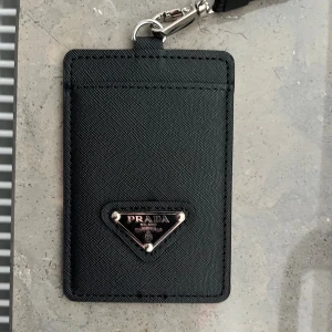 Svart korthållare - Tjena, säljer en snygg svart korthållare från P*ada. Riktigt snygg och stilren och passar till alla kläd stilar. Själva korthållare sitter fast med ett snöre som man kan ha runt halsen. Den är helt ny! Har du någon fråga bara hör av dig ☺️