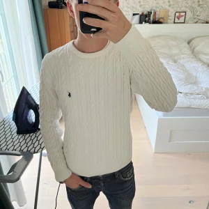 Vit kabelstickad tröja Ralph Lauren - Snygg vit kabelstickad tröja från Ralph Lauren med klassisk rund hals och broderad logga på bröstet. Tröjan har långärmad passform och är gjord i mjuk bomull. Perfekt för dig som gillar clean och stilren look. Storlek M men passar S-Xs jag är 177cm och väger 62kg, tröjan är lite liten på mig.