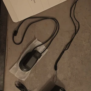  Actionkamera - Smidig och lätt actionkamera med roterbar design, perfekt för vloggning och äventyr. Utrustad med display och halsrem för enkel användning. Kameran ser ut att vara i mycket gott skick utan synligt slitage. Stöd för WiFi och flexibel montering.