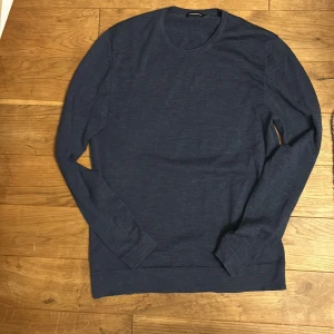   J.Lindeberg merinoull - Snygg mörkblå långärmad tröja från J.Lindeberg med diskret broderad logga på bröstet. Tröjan har rund halsringning och är tillverkad i mjuk bomull, perfekt för en clean och stilren look. Storlek M