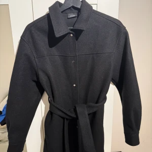 Svart medellång kappa  - En väldigt fin svart medellång kappa köpt på vero Moda. Den har ett väldigt skönt och mjukt material. Den har ett knytband så man kan knyta kappan. Kappan är använd 1 gång och är i mycket bra skick. Den värmer och passar väldigt bra till både hösten och våren🤍