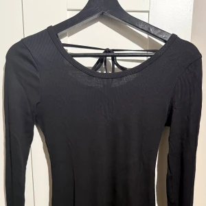 Svart långärmad klänning  - En fin svart ribbad klänning. Den har ett väldigt mjukt och skönt material som varken sticks eller är för tjockt. Den är öppen i ryggen och har ett knytband. Den har endast använts en gång och är i mycket bra skick utan några skador. Klänningen slutar ungefär precis vid knäna. Den passar perfekt till fina event eller middagar. Säljer den då den inte kommer till användning🤍