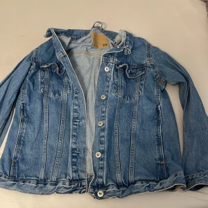 Blå jeansjacka från 157, storlek M - Klassisk blå jeansjacka från 157 i storlek M. Jackan har knappar framtill, två bröstfickor med lock och snygga söm-detaljer. Tillverkad i slitstarkt denim med en tidlös look som passar perfekt till din streetstyle.