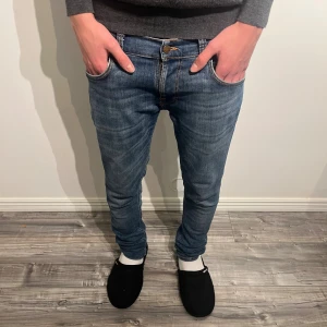 Blå Nudie Jeans 30/32 - Snygga blå jeans från Nudie Jeans i modellen Slim med klassisk femficksdesign och orangea sömmar. Jeansen har en smal passform, normal midja och är tillverkade i mjukt jeanstyg. Perfekt för dig som gillar en modern och stilren look.