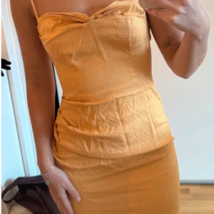 Orange bomullklänning med smala axelband - Säljer en snygg gul kort klänning med smala axelband och figurnära passform. Klänningen har en enkel design med lätt drapering vid midjan och en något asymmetrisk nederkant. Perfekt för dig som gillar färg och vill sticka ut. 