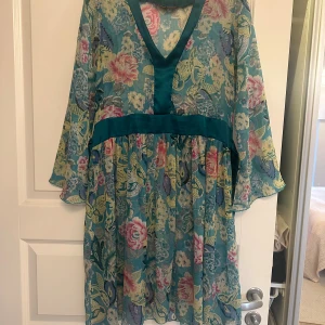 Blommig tunika Uttam London - Säljer en blommig tunika från Uttam London i turkos och gröna toner med inslag av rosa, gul och blå. Tunika har v-ringning och trekvartsärmar. Materialet är lätt och luftigt, perfekt för varma dagar. Snyggt band i midjan för extra form.
