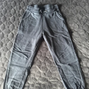 Mörkgrå mjukisbyxor med snörning - Mörkgrå mjukisbyxor från lager 157 med ribbad midja och snörning. Byxorna har två sidofickor och muddar vid bensluten för extra komfort. Materialet är mjukt och fleece-liknande på insidan, perfekt för chill dagar. Snygg och enkel design som passar till hoodies och sneakers.