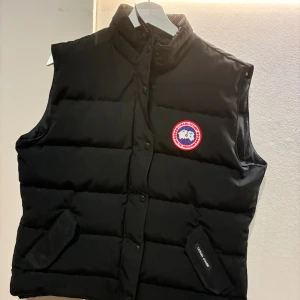 Svart dunväst med röd logo  - Svart dunväst i storlek XL men passar bättre L/M.  hög krage och tryckknappar framtill. snygg att styla över hoodie. Pris går er diskutera!