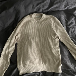Beige stickad tröja från Kappahl - Säljer en beige stickad tröja från Kappahl med ribbad struktur och rund hals. Tröjan har långärmade ärmar och en klassisk, enkel design som är lätt att matcha med olika outfits. Perfekt för dig som gillar stilrena och neutrala plagg.