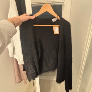 Svart fluffig kofta från ASOS - Mysig svart kofta från ASOS med fluffig och mjuk känsla. Koftan har långärmade ärmar och en öppen front utan knappar. Perfekt för att ge din outfit en chill och trendig vibe. Passar dig som gillar tröjor som är bekväma och inte sticks! Köpt på sellpy men aldrig använt🌞 hör av er om frågor!