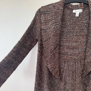 Brunmelerad draperad kofta från Dressbarn - Mysig brunmelerad stickad kofta från Dressbarn med vacker drapering som är lite kortare framtill och går nedanför rumpan baktill. Långa ärmar, bred krage, varm och mysig samtidigt som den är snygg och lite annorlunda.