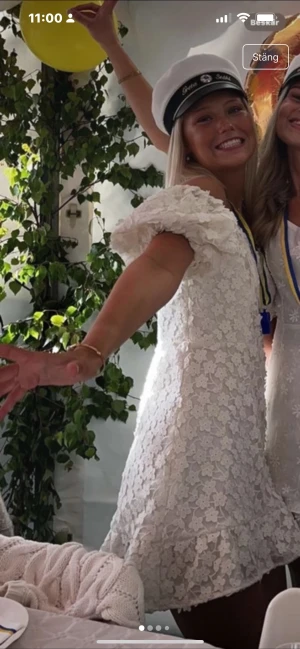 Vit blommig offshoulder studentklänning - Superfin vit kortklänning med blommigt spetsmönster och volangkant. Offshoulder-modell med puffiga korta ärmar som ger en romantisk vibe. Perfekt till student eller sommarens alla tillfällen. Sitter snyggt och har en lätt utsvängd passform.