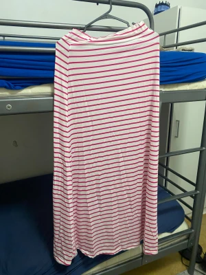 Vit långkjol med rosa ränder - Vit lång kjol med tunna rosa horisontella ränder. Kjolen har en rak och lös passform. Perfekt för dig som gillar en enkel men ändå lekfull stil.