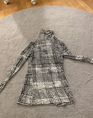 Svartvit polotopp från H&M XS - Säljer en svartvit polotopp från H&M i storlek XS. Toppen har ett coolt rutigt mönster med lång ärm och hög krage. Materialet är mjukt och stretchigt, perfekt för att styla med jeans eller kjol. Snygg passform som sitter tight och markerar siluetten.