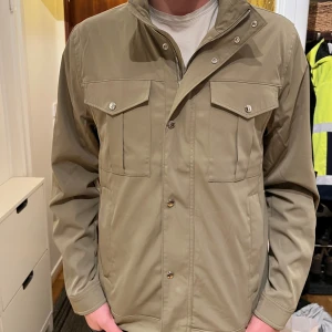 J.Lindeberg jacka (LAPPEN KVAR!) - Helt ny, oanvänd snygg ljus Olivgrön vindjacka/fieldjacket från J.Lindeberg i storlek XL. Jackan har ståkrage, tryckknappar framtill, fyra fickor med lock och en diskret svart patch på ärmen. Galant för höstdagar och även till våren. Köpt för 3400kr (nypris) och lappen sitter kvar, helt nyskick då jag beställde hem fel och aldrig använd. Bredd över Axlarna 51cm, Längd 72cm. Han på bild 1 & 2 är ca 190cm. Priset är inte hugget,kom med bud och tveka inte på att höra er! 
