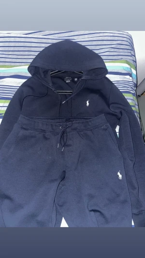 Polo Ralph Lauren - Säljer en mörkblå hoodie från Polo Ralph Lauren med klassisk huva och dragsko. Så gott som ny äkta såklart kvitto finns. Koftan är i storlek xs och byxorna i s 