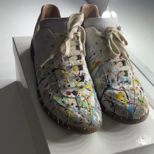 Maison Margiela paintsplatter skor - Maison Margiela Paint Splatter sneakers, storlek 40 men passar även 41. Mycket bra skick med endast lite smuts som kan torkas bort och ett litet märke på sulan. Box, dustbags och kvitto finns, allt og ingår! Jag köpte dem på rea hos Merch, och kvittot finns på sista bilden, nypris ca 7 tusen. Skriv gärna vid frågor eller om du vill ha fler bilder. Priset kan diskuteras 🤝 