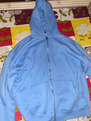 Ljusblå hoodie med dragkedja - Ljusblå hoodie med hel dragkedja framtill och stor huva. Tröjan har två rejäla fickor och är tillverkad i mjuk fleece som känns skön mot huden. Perfekt för chill dagar och när du vill ha något bekvämt och enkelt. Passar dig som gillar en loose fit.