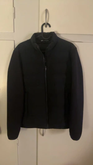 Svart pufferjacka från Zara - Svart pufferjacka från Zara med stilren design och rak passform. Jackan har hög krage och dragkedja framtill. Perfekt för kyliga dagar och enkel att matcha med olika outfits.