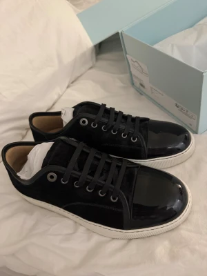 Lanvin - Svart - Lanvin Paris sneakers i svart mocka med glansig tå i lack och vita platta gummisulor. Klassisk rund tå, snörning med svarta skosnören och metallöglor. Snygg kontrast mellan material och färg, levereras med originalkartong och dustbag + kvitto finns. Använda 1 gång därav smuts under sulan.