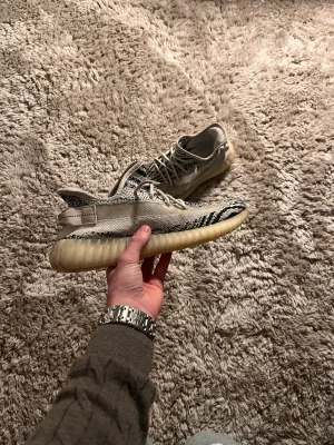 Adidas Yeezy Boost 350 Zebra sneakers - Säljer ett par Adidas Yeezy Boost 350 'Zebra' sneakers med svartvitt zebramönster och vit sula. Skorna har snörning, rund tå och en stickad ovandel i syntetmaterial. Den ribbade plattformssulan ger en unik look och extra komfort. Perfekt för dig som gillar streetwear.