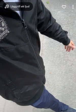 Norra stå jacka - Svart vindjacka med dragkedja framtill och emblem på bröstet. Jackan har ribbade muddar vid ärmslut och nederkant samt praktiska sidofickor. Tillverkad i lätt polyester som passar perfekt för blåsiga dagar.