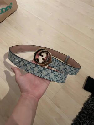 GG blått bälte - Säljer ett GG bälte med klassiskt blått monogrammönster och stor rund guldspänne med GG-logga. Bältet är i blå färg, tillverkat i skinn med canvas-yttermaterial. Perfekt accessoar för att lyfta din outfit.