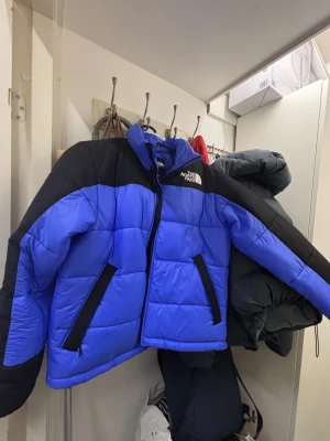 Blå pufferjacka från The North Face - Säljer en blå och svart pufferjacka från The North Face i storlek M. Jackan har hög krage, dragkedja framtill och två fickor med svarta detaljer. Perfekt för kalla dagar och riktigt snygg streetstil. Den passar ej min hudfärg så vill bli av med den den är köpt nyligen men tog bort prislappen, använd 2 gånger ena som prov inget fel eller skada på jackan som helt ny i sick.