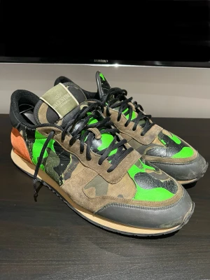 Valentino Rockrunners - Säljer ett par Valentino Rockrunner sneakers med grön och brun camouflage, orange mockadetalj vid hälen och svarta snören. Skorna är väl använda fast har en del kvar i sig, perfekt om man vill ha ett par unika skor. Skorna är såklart äkta. Hör av er vid minsta funderingar!