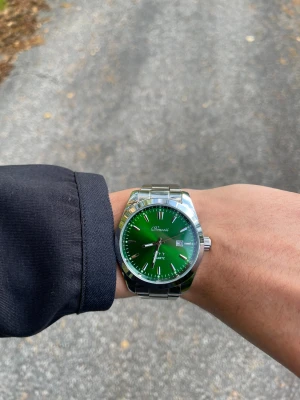 Grön klocka från Doventi med stållänk - Snygg klocka från Doventi med grön urtavla och datumvisning. Klockan har en rund boett i silverfärgat stål och matchande länkarmband. Stilrena indexmarkeringar och quartz-urverk gör den både modern och enkel att bära till olika outfits.