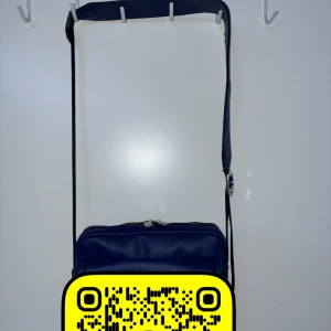 Mörkblå axelväska i skinn - Säljer en stilren mörkblå axelväska i skinn med justerbar rem och dragkedja upptill. Väskan har en fyrkantig form och är perfekt för att bära det viktigaste. Enkel och clean design som passar till många outfits.