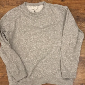Grå sweatshirt från H&M Essentials - En stilren grå sweatshirt från H&M Essentials, modell No 5, i relaxed fit. Tröjan har rund hals, långa ärmar och mjukt, fleeceliknande foder på insidan. Perfekt för chill dagar och enkel att matcha med jeans eller joggers.