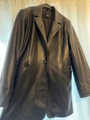 Svart skinnkavaj från BikBok M - Säljer en svart skinnkavaj från BikBok i storlek M. Jackan har klassisk krage, en knapp framtill och två fickor. Snygg oversized look och tillverkad i mjukt material som ger en cool vibe till din outfit.