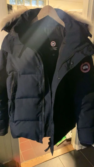 Äkta Mörkblå Canada Goose dunjacka med päls - Säljer en mörkblå dunjacka från Canada Goose med ikonisk patch på ärmen och fluffig beige päls på huvan. Jackan har dragkedja, knappar och flera fickor. Perfekt för kalla vinterdagar och har en riktigt schysst oversized look. Finns kvitto påse och allt.