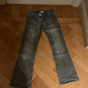 Grå jeans med raka ben från Gina Tricot - Grå jeans från Gina Tricot med raka ben och coola slitningar. Byxorna har framfickor med lock och markerade sömmar längs benen. Klassisk femficksmodell och knappstängning framtill. Perfekta för en avslappnad och trendig look.