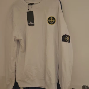 Vit Stone Island sweatshirt XL - Vit sweatshirt från i storlek XL. Klassisk rund hals, långärmad modell med ikoniska loggan på bröstet och avtagbar patch på ärmen. Tillverkad i mjuk bomull för en clean och stilren look. Mer som L.