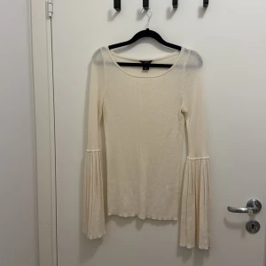 Ribbad beige tröja med trumpetärm - Supersnygg ribbad beige tröja från Lindex med lång trumpetärm och rund hals. Tröjan har en slim passform och är tillverkad i mjukt stickat material som känns skönt mot huden. Perfekt för dig som gillar unika detaljer på ärmarna.